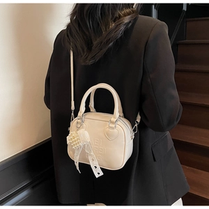 Dettaglio borsa a tracolla beige con toppa a cuore e ciondolo in perle di pizzo