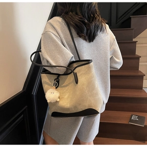 Detail of khaki suede tote bag with black leather trim and white plush charm on model