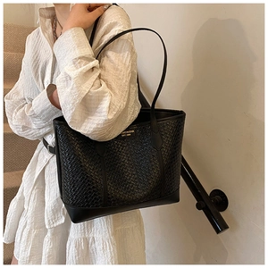 Détail du sac cabas tressé noir montrant la texture géométrique et le logo doré sur le côté