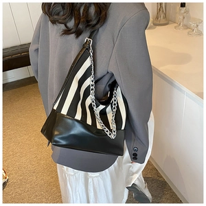 Detail of striped canvas shoulder bag with black leather trim and silver chain on model