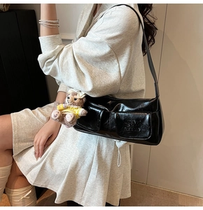 On-body view of a shiny black patent leather underarm bag with cute plush bear pendant