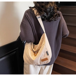 Close-up of beige canvas crossbody bag with wide adjustable strap and brand logo labels