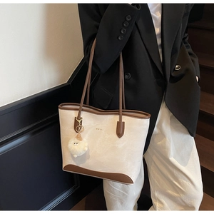 Detail of minimalist tote bag featuring gold logo, brown leather trim, and white fur charm