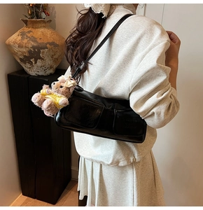 Detail of black glossy faux leather underarm bag with cute teddy bear charm on strap