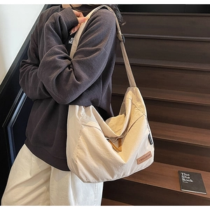 Close-up of beige canvas messenger bag with adjustable strap and leather logo tag