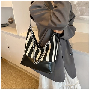 Close-up of black and white striped canvas tote bag with silver chain strap worn by a model