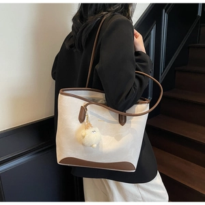 Detail of minimalist cream tote bag with brown trim and plush sheep charm on a shoulder