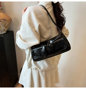 Close-up of black baguette bag featuring glossy wrinkled leather and dual front pockets