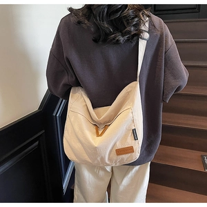 Detail of cream canvas messenger bag with brown leather brand tag and fabric texture