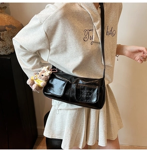 Detail of glossy black underarm bag with cute teddy bear charm and functional pockets