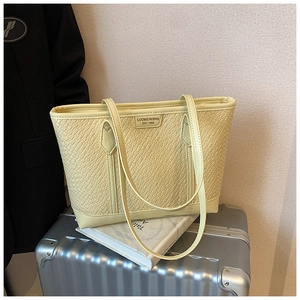 Détail de la texture tressée et du logo métallique sur un grand sac cabas jaune pâle