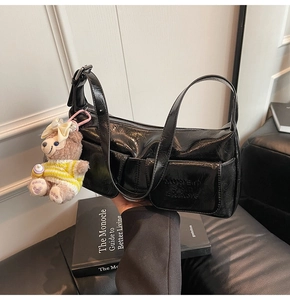 Detail of black glossy pleated underarm bag featuring dual pockets and cute bear charm