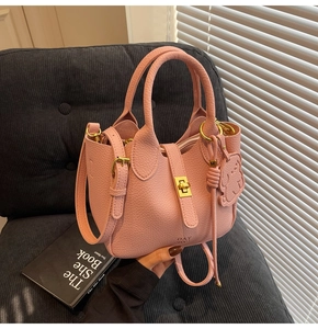 Detail of pink lychee leather handbag featuring gold turn-lock and cute bear charm