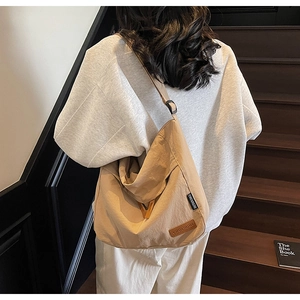 Detailed back view of a large beige canvas crossbody bag on a model in a cozy staircase setting