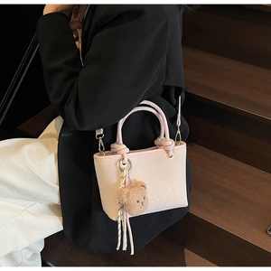 Detail of pink woven bucket bag with brown bear charm and tassel on a chic model
