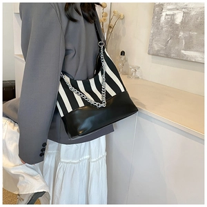 Detail of striped canvas and leather shoulder bag with chunky silver chain on model