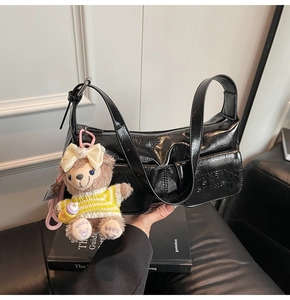 Detail of black patent leather shoulder bag featuring crinkle texture and cute bear charm