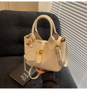 Close-up of off-white lychee leather handbag with gold twist lock and dog charm