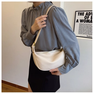 Close-up of cream textured leather crescent bag with adjustable strap and metal hardware