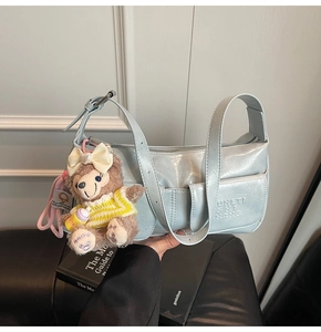 Detail of light blue pleated patent leather baguette bag with adorable teddy bear charm