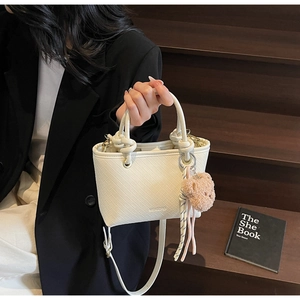 Close-up of white woven bucket bag with knotted handle and pink plush bear charm