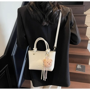 Detailed view of white woven bucket bag with MEIGERE logo and brown bear pendant accessory