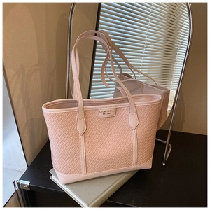 Détail du sac cabas rose gaufré crocodile avec plaque de logo dans une lumière douce