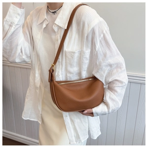 Detailed close-up of brown litchi grain leather shoulder bag worn by model in white