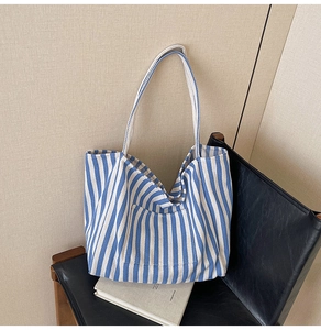 Detail of blue striped canvas tote bag showing the front pocket and long shoulder straps