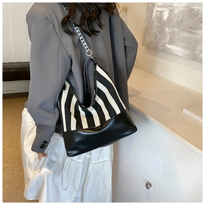 Detail of a large black and white striped tote bag with silver chain strap worn by a model