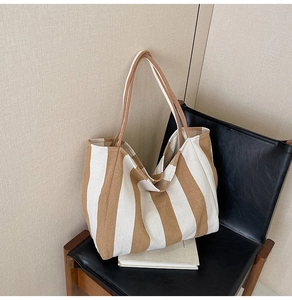 Detail of a large striped canvas tote bag resting on a leather chair in a home setting