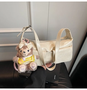 Detail of creamy textured leather shoulder bag with logo embossing and plush bear charm