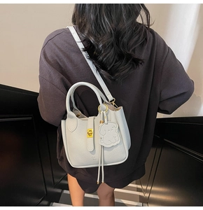 Detail of lychee pattern leather bucket bag with gold hardware and dog charm on a model