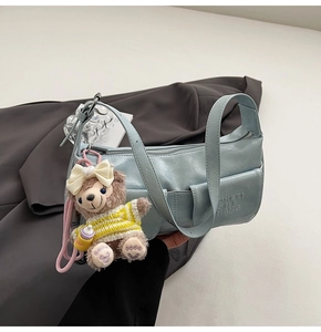 Detail of light blue faux leather underarm bag with embossed letters and plush bear charm