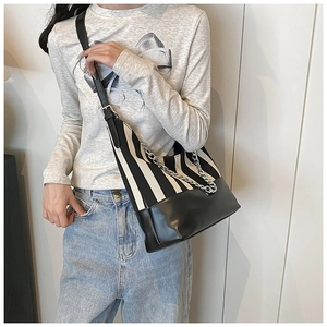 Detail of black and white striped canvas shoulder bag with silver chain strap on model