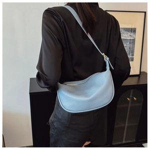 Detail of light blue crescent saddle bag with pebble leather texture and gold metal clasp