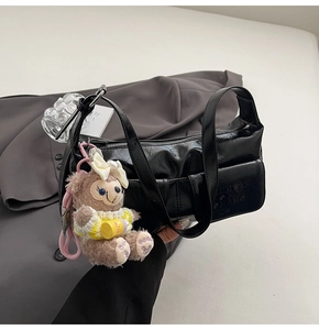 Detail of black glossy shoulder bag with textured pocket and cute brown teddy bear charm