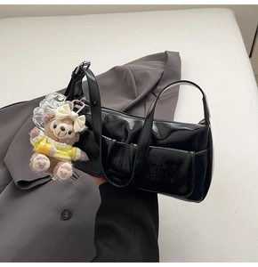 Close-up of black patent leather underarm bag with zipper pocket and plush bear charm