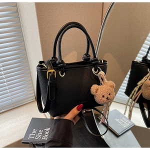 Detail of black woven texture handbag featuring a plush bear charm and metallic hardware