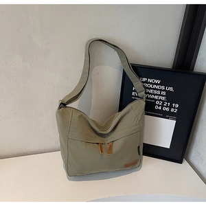 Detail of olive green nylon tote bag with zippered front pocket and brown leather logo tag