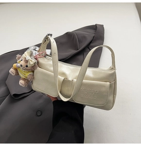 Detail of cream white underarm bag showing glossy leather texture and cute bear charm