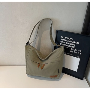 Detail of olive green nylon tote with leather logo and dual zippers on white surface