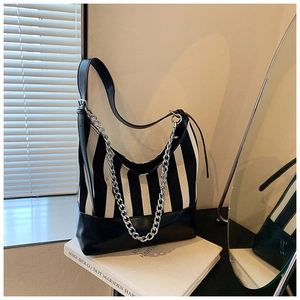 Detail of striped canvas shoulder bag with silver chain on art books with light and shadow