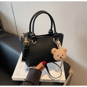 Detail of black woven texture bucket bag with gold hardware and plush bear charm
