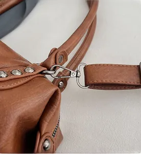 Detail of silver hardware lobster clasp and metal rivets on dark brown leather tote bag