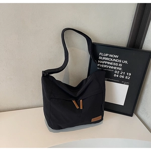 Close-up of black canvas messenger bag with brown zipper pulls and leather logo detail