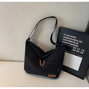 Detail of black nylon messenger bag featuring adjustable strap and leather logo patch