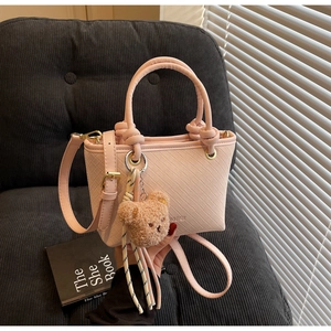 Detail of light pink woven bucket bag with knot handles and a brown plush bear charm