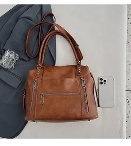 Detail view of large brown faux leather tote bag with silver hardware and phone for scale