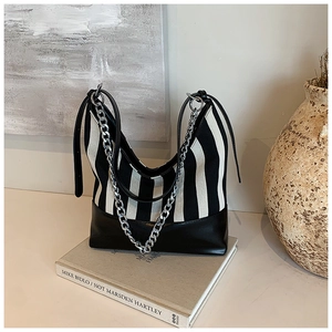 Detail of striped canvas tote bag with black leather base and silver chain strap